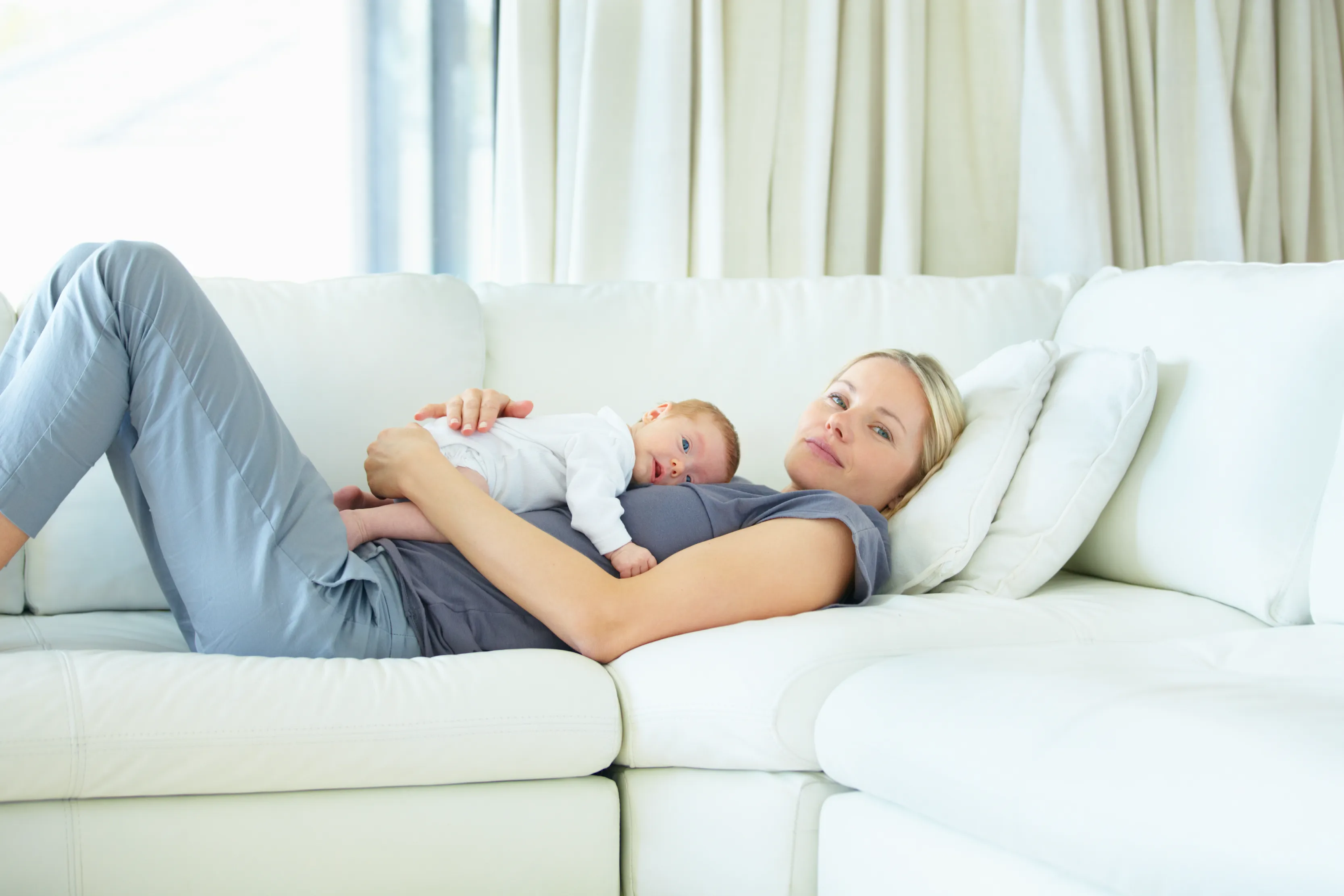 A mother resting comfortably at home with her newborn baby.